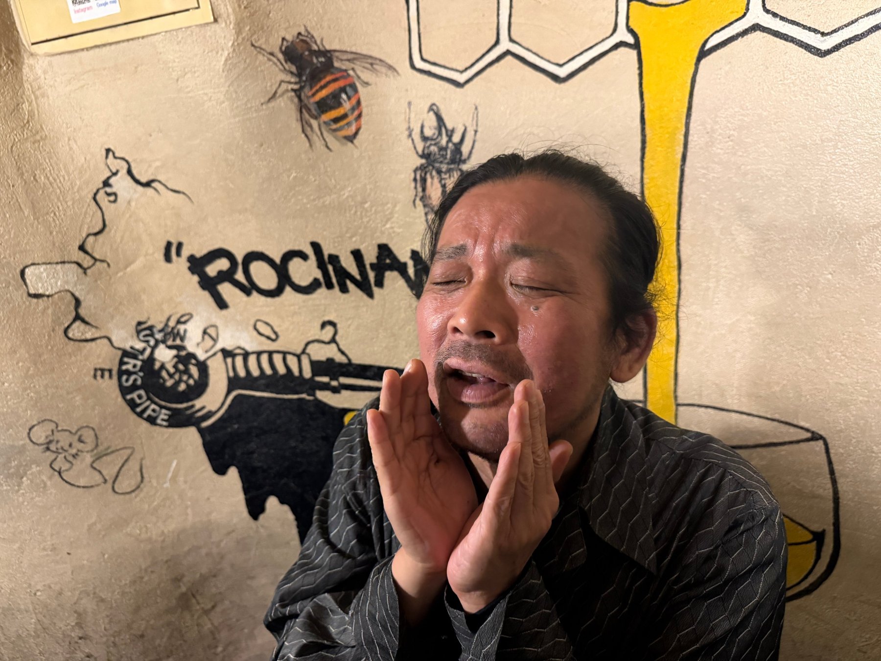 店名の壁画の前で口元に手を添える人